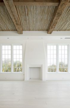 an empty white room with three windows and a fire place in the center is surrounded by wood beams