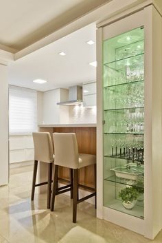 a kitchen with a bar and some chairs in front of the glass shelves that have wine glasses on them