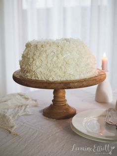 a white cake sitting on top of a wooden platter next to a lit candle