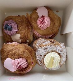 four pastries in a white box with pink icing