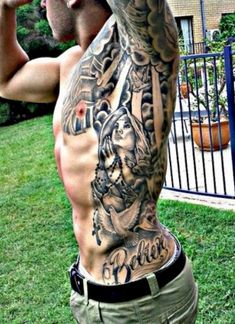 a man with tattoos on his back standing in the grass