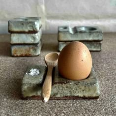 an egg sitting on top of a stone block next to two spoons and salt shakers