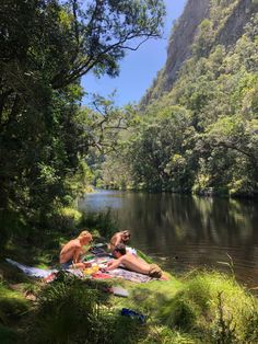 two people are sitting on the bank of a river