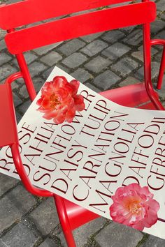 a red chair sitting on top of a brick floor next to a sign with flowers