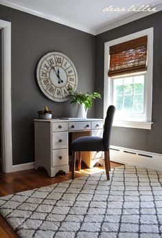 a desk with a chair and a clock on the wall above it in front of a window