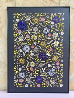 an intricately designed painting with flowers and leaves on a black frame against a stone wall