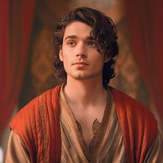 a young man with curly hair wearing an orange and gold outfit, looking at the camera