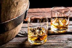 two glasses filled with whiskey sitting on top of a wooden barrel