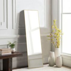 a large mirror sitting on top of a floor next to a vase with flowers in it