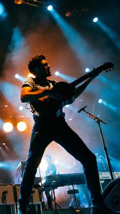 a man standing on top of a stage with a guitar in his hand and lights behind him