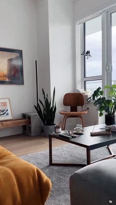 a living room filled with lots of furniture and plants on top of a table in front of a window