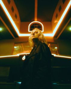 a woman standing in front of a building with neon lights on it's ceiling