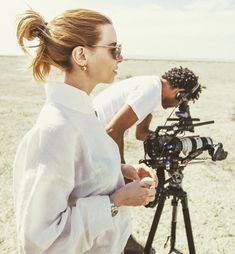 a woman standing next to a camera on top of a sandy beach