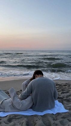 a woman sitting on top of a beach next to the ocean with her head in her hands