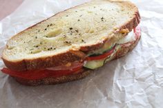 a sandwich with tomato, cheese and cucumber on it sitting on wax paper