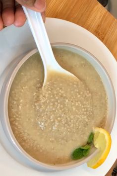 a person is holding a spoon in a bowl of oatmeal with lemon and mint