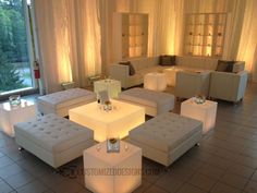 a living room filled with white couches and tables covered in lights next to windows