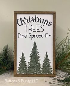 a christmas tree sign sitting on top of a wooden shelf next to evergreen branches and pine cones