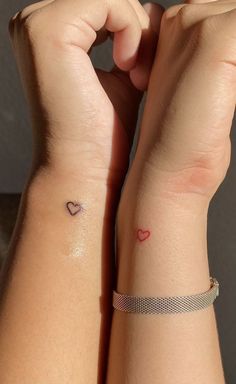 two people with matching tattoos on their arms and wristbands, one has a small heart tattoo on the other arm