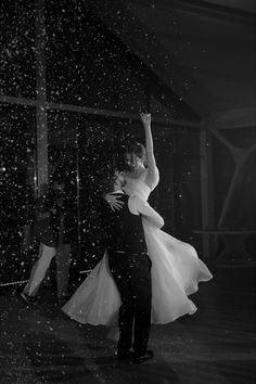 a bride and groom are dancing in the rain at their wedding reception, black and white photo