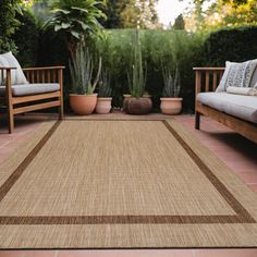 an outdoor area with two couches and a rug on the ground in front of some plants