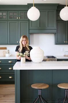 a woman standing in front of a kitchen island with two vases on top of it