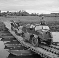 an army vehicle driving across a bridge with two men on it's back in the water