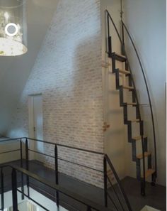 a stair case in the corner of a room next to a brick wall and metal handrail