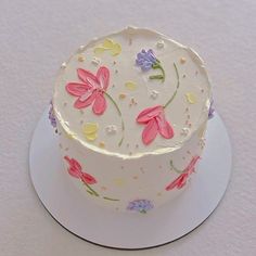 a white cake with pink and purple flowers painted on the top is sitting on a plate