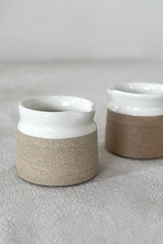 two white and brown vases sitting on top of a gray cloth covered tablecloth