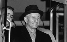 black and white photograph of two men sitting next to each other, one wearing a hat