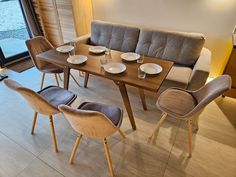 a dining table with four chairs and plates on it in front of a large window