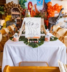 a table topped with an easel and a drawing on top of a white table cloth