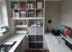 a computer desk sitting in front of a window next to a white shelf filled with books