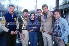 a group of young men standing next to each other in front of a parked car