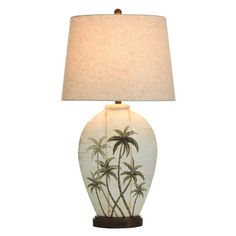 a table lamp with a palm tree design on the bottom and a beige shade over it