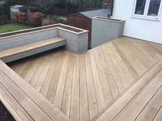 a wooden deck with benches and planters in the back yard, next to a house