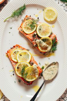 two pieces of salmon on a plate with lemons and dill garnish