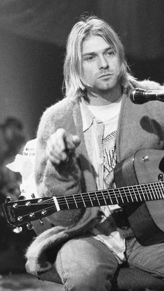 a man holding a guitar while sitting in front of a microphone