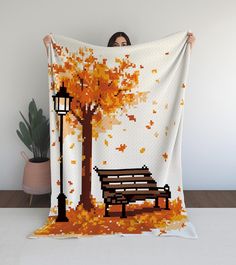 a woman is holding up a blanket with an image of a bench and tree in autumn