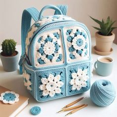 a crocheted backpack sitting on top of a table next to yarn and knitting needles