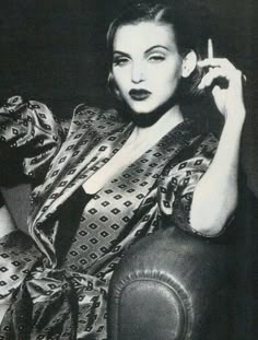 a black and white photo of a woman sitting in a chair with her hand on her hair