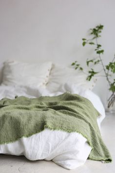 an unmade bed with green and white linens on the sheets, next to a potted plant