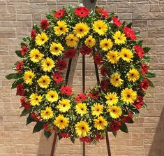 a wreath with yellow and red flowers in front of a brick wall on a stand