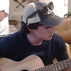 a man wearing a hat and playing an acoustic guitar in a room with couches