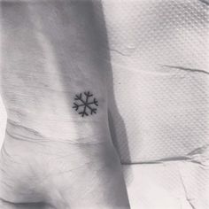 a small snowflake tattoo on the left side of the foot, with an arrow at the center