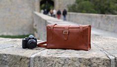 a brown leather bag sitting on top of a stone wall next to a black camera