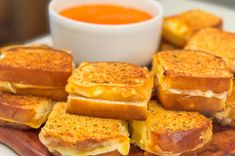 several grilled cheese sandwiches on a wooden platter with a bowl of tomato soup