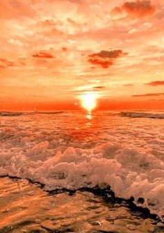 the sun is setting over the ocean with waves crashing in front of it and an orange sky