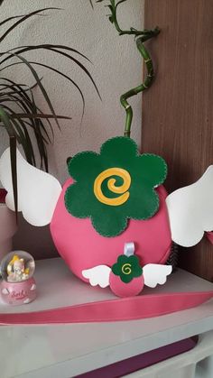 a pink and green apple with angel wings on a shelf next to a potted plant